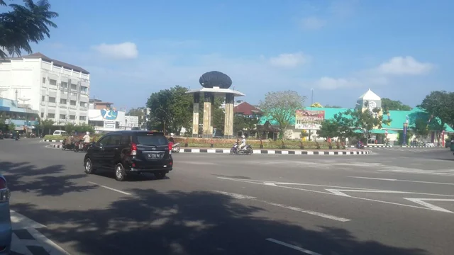 Kendaraan melintasi jalan dan bundaran di pusat Tanjungpandan, dengan bangunan pertokoan di sekelilingnya.